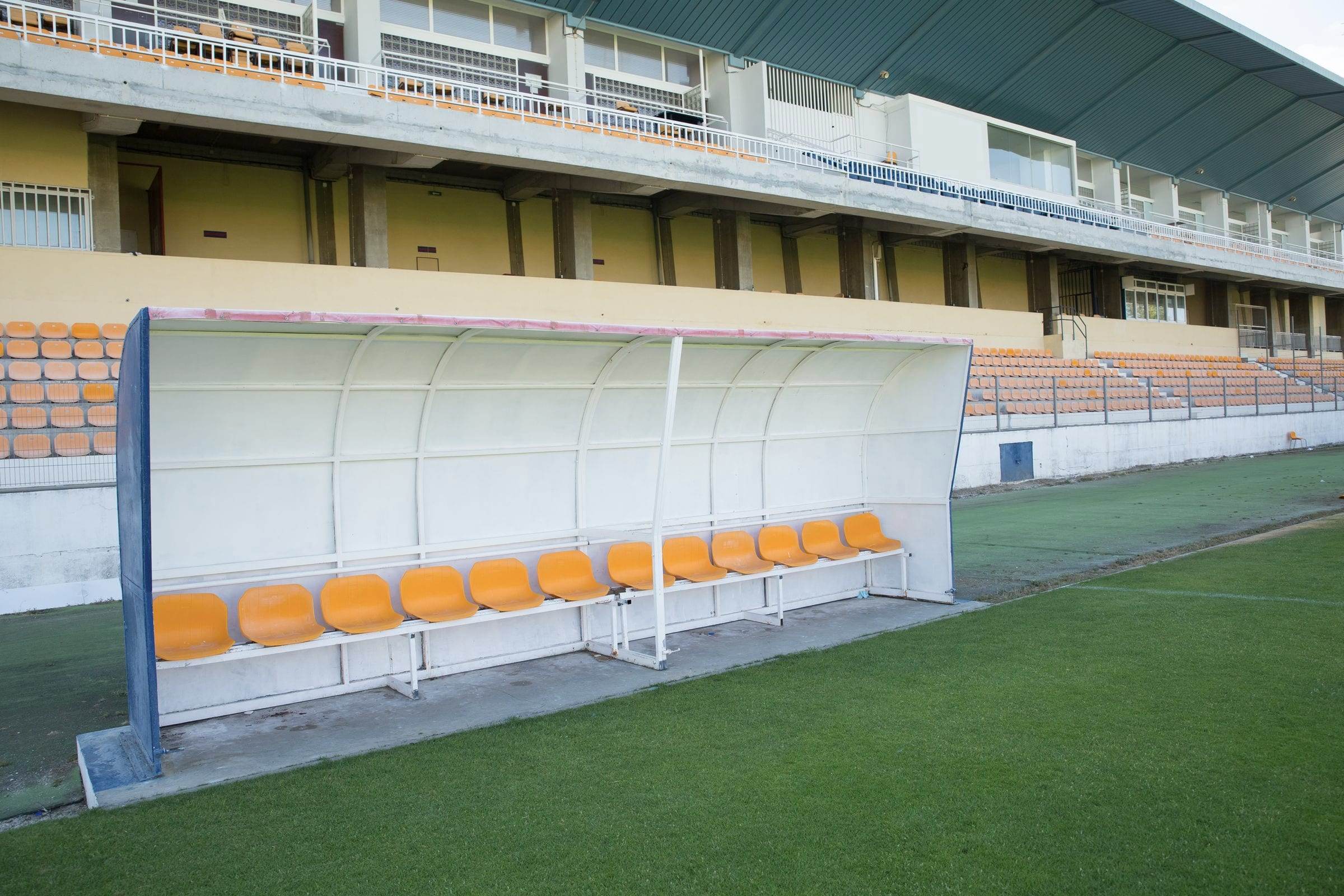 Banc de touche vide au bord d’une pelouse, tribune en arrière-plan
