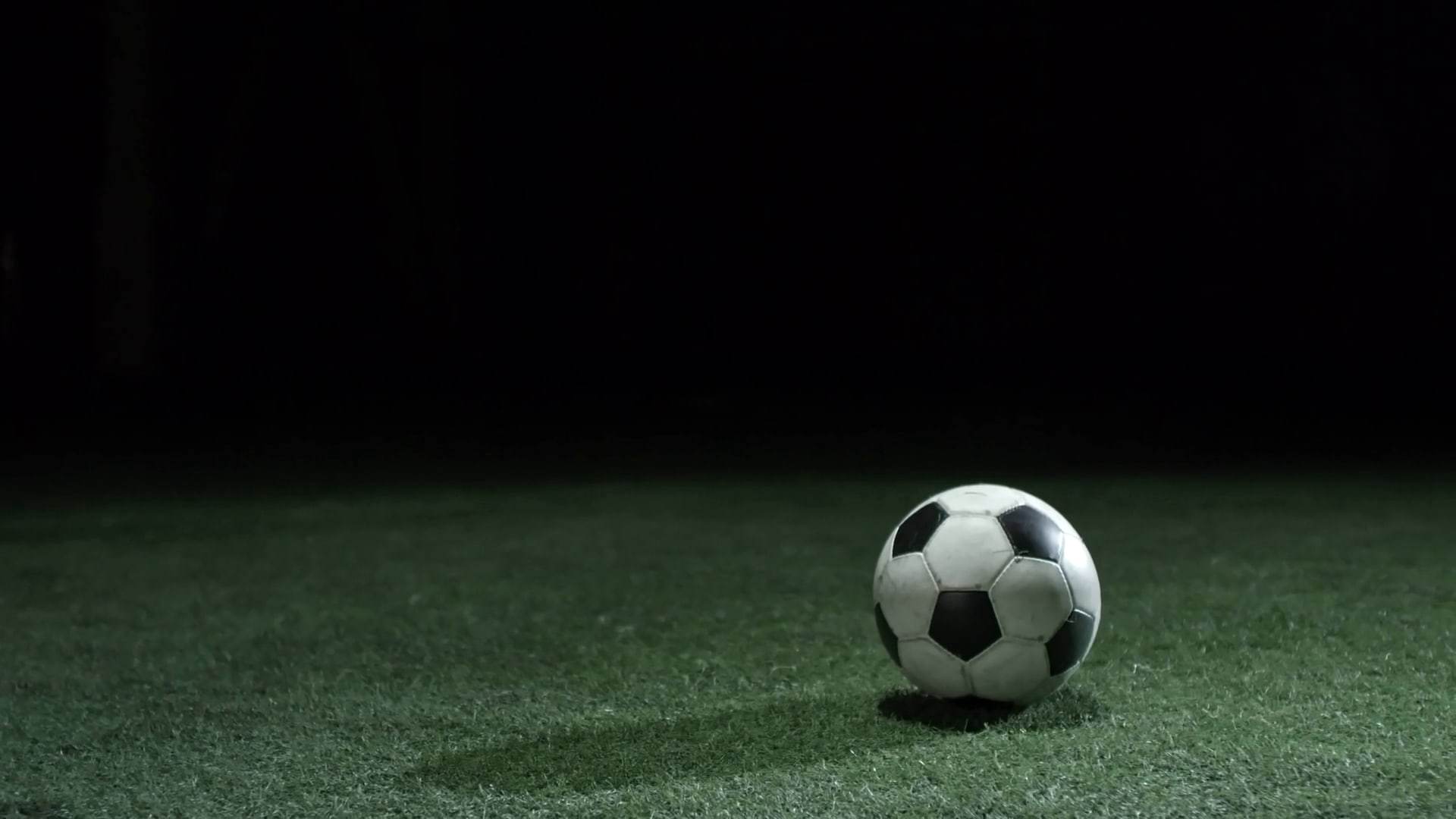 Ballon de football posé sur une pelouse éclairée, de nuit